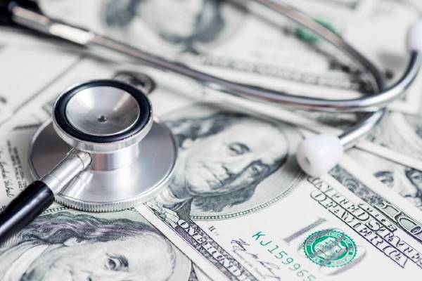 A stethoscope on top of a pile of one hundred dollar bills.