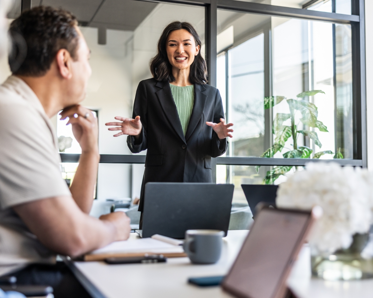 Two professionals with laptops have a meeting in a bright office with large windows