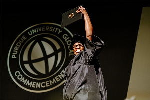 A graduate holds a Purdue Global diploma at a commencement ceremony.