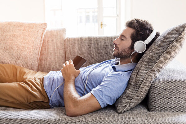A man takes a break from his studies by reclining on a couch and listening to music.