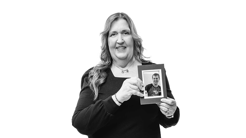 Black and white photo shows Wilson smiling and holding a framed photo of her son, Nick.