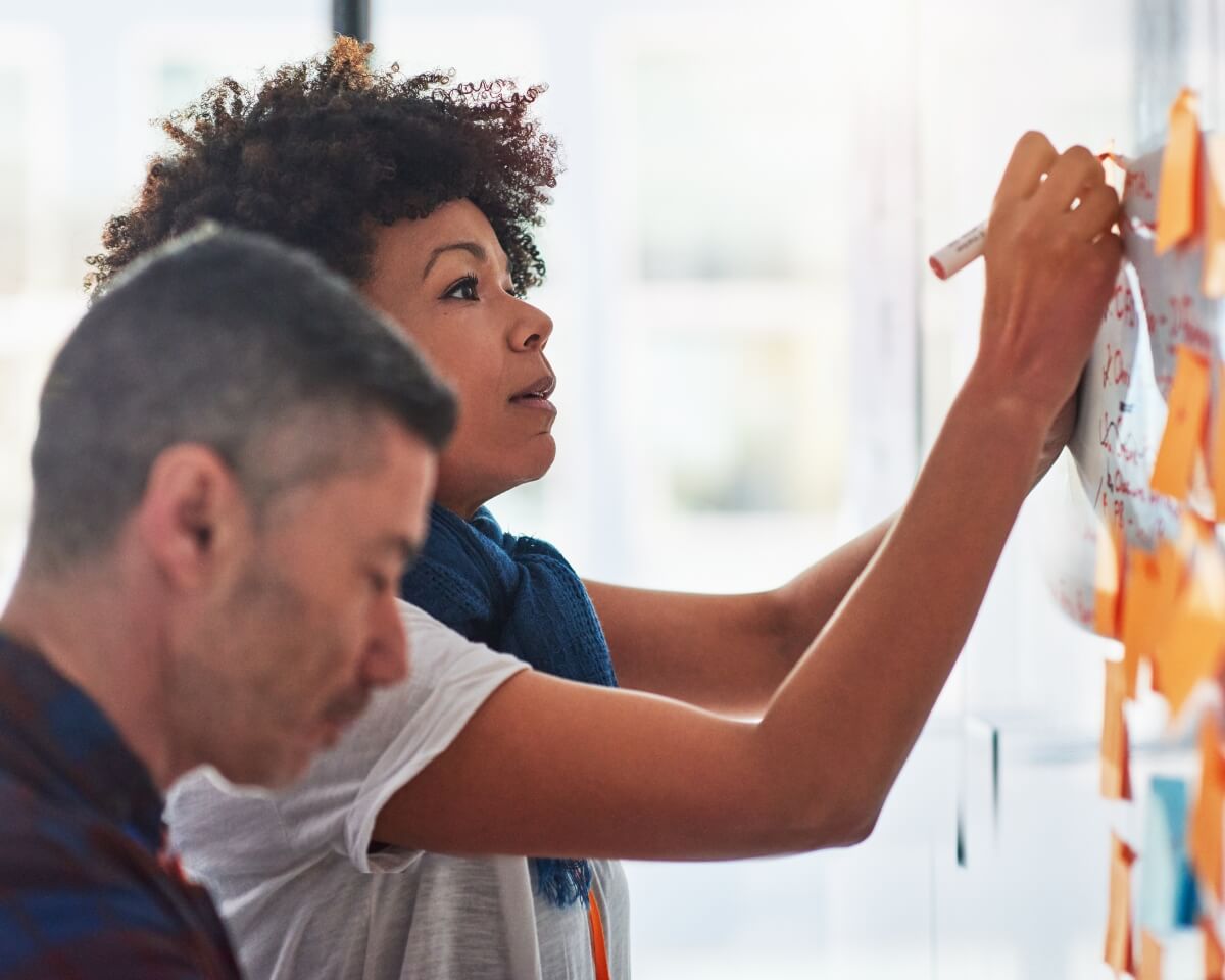 Business colleagues reviewing sticky notes on a glass wall during a collaborative planning session in a bright office space