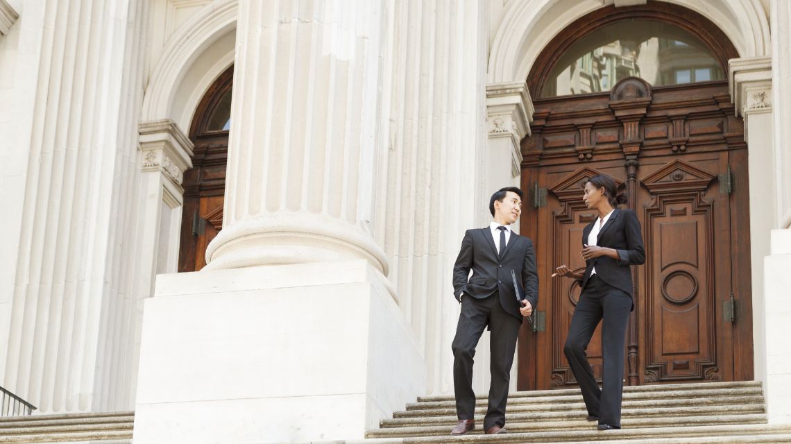 Two attorneys have a conversation on the steps of a courthouse.