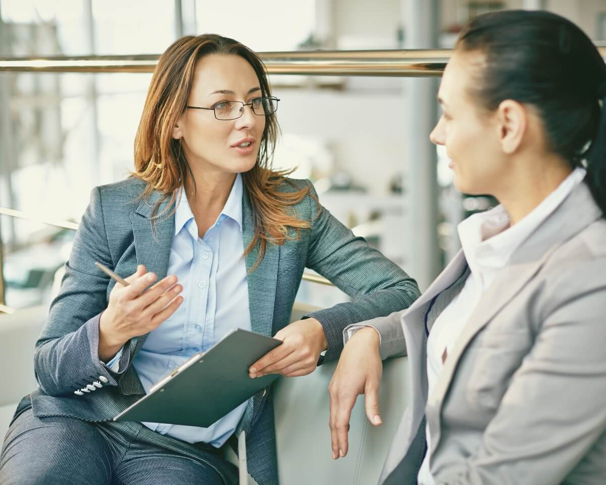Two professionals engaged in conversation; one taking notes on a device