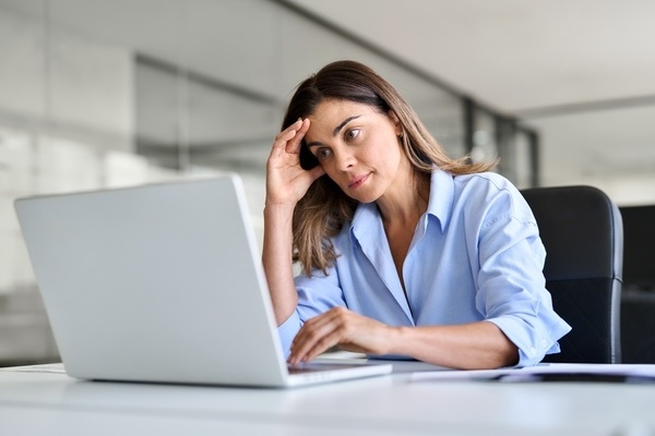 A woman looking at a laptop while deep in thought.