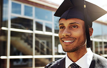man in graduation cap outside modern glass building