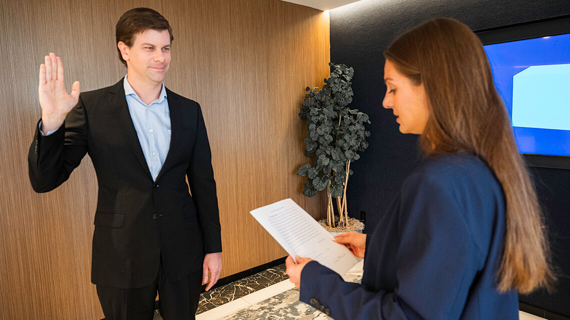 alt: Ryan Bormann is sworn in by a colleague in an office.