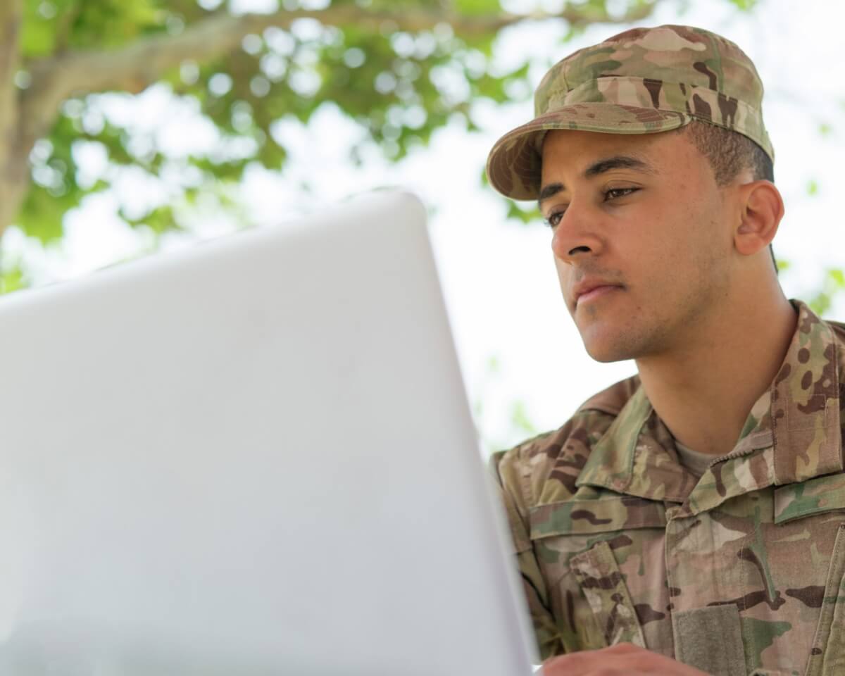Military servicemember in uniform working on a laptop outside