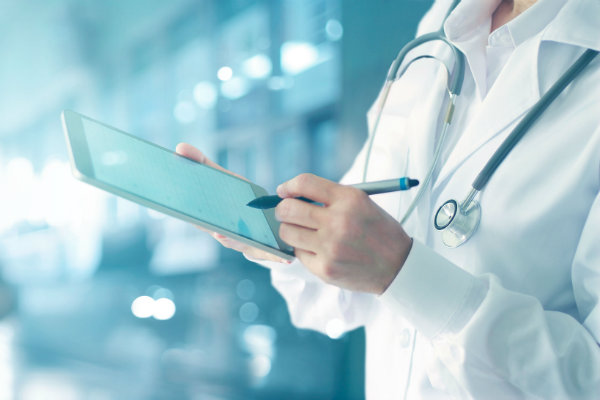 Health professional with stethoscope making notes on an electronic tablet