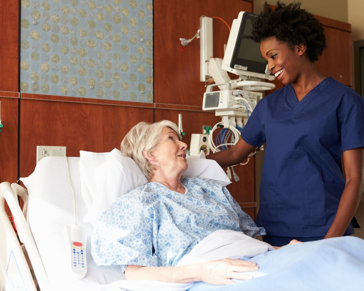 A nurse smiles at an elderly patient in a hospital bed