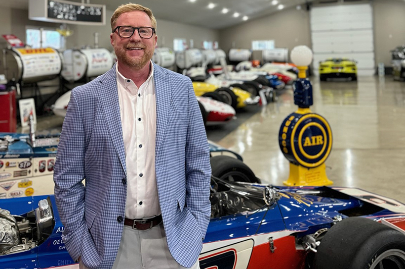 Michael Good standing next to race cars in a large garage
