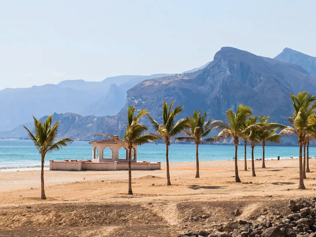 Oman, Dhofar, Salalah Palmenstrand mit Pavillon vor Bergen. Salalah, Dhofar, Oman.