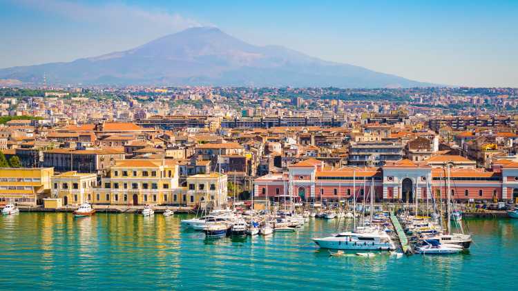 Europe - Italy - Sicily - Coast of Catania cruise port seen from the bat, blue skies and blue ocean and smoking volcano.