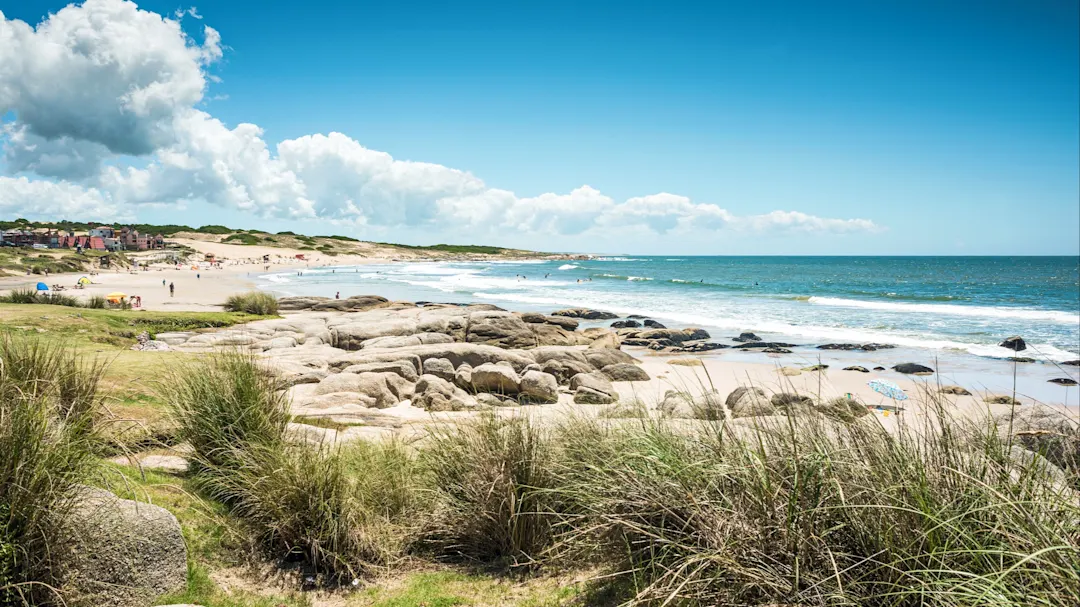 Punta del Diablo, Strand, Uruguay Strand mit weichem Sand, Felsen und grünen Dünen unter klarem Himmel. Punta del Diablo, Rocha, Uruguay.