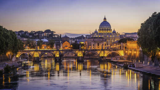 Europe, Italy, Rome, St Peters Basilica is seen from the Tiber River as the sunset casts the scene in purple and orange light.