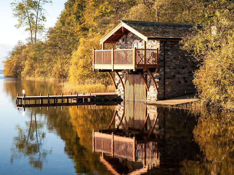 Ullswater, Lake District, England Bootshaus am See mit Herbstbäumen und Bergen im Hintergrund, Ullswater, Lake District, England.