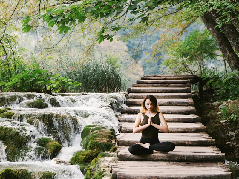 Japon, Yoga Femme méditant sur une passerelle en bois au-dessus d'une cascade. Japon.