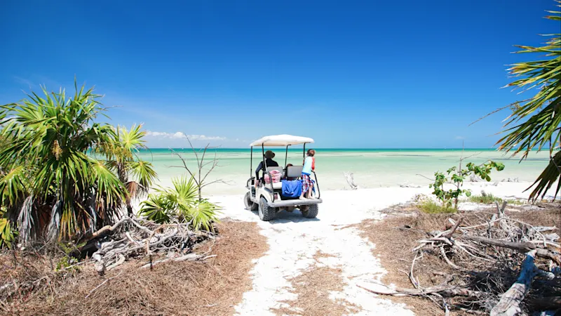 Golfwagen Golfwagen fährt zu einem tropischen Strand.