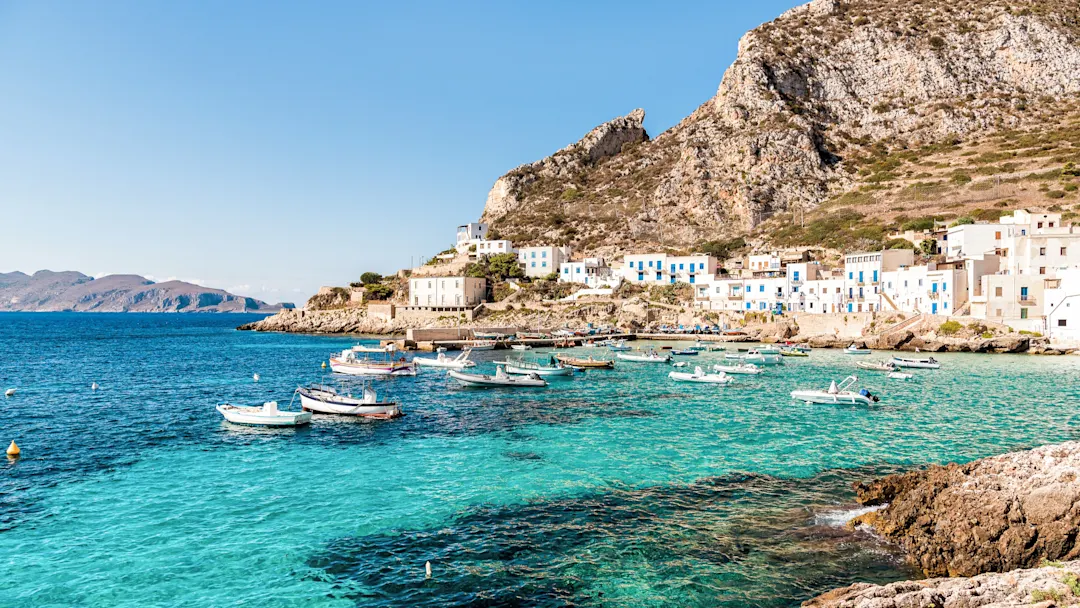 Boote im klaren Wasser vor dem Küstendorf, Trapani, Sizilien, Italien.
