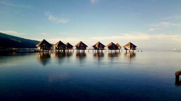 Magnifique coucher du soleil sur des bungalows de vacances sur pilotis en pleine mer dans lesquels séjourner pendant votre voyage à Tahiti.