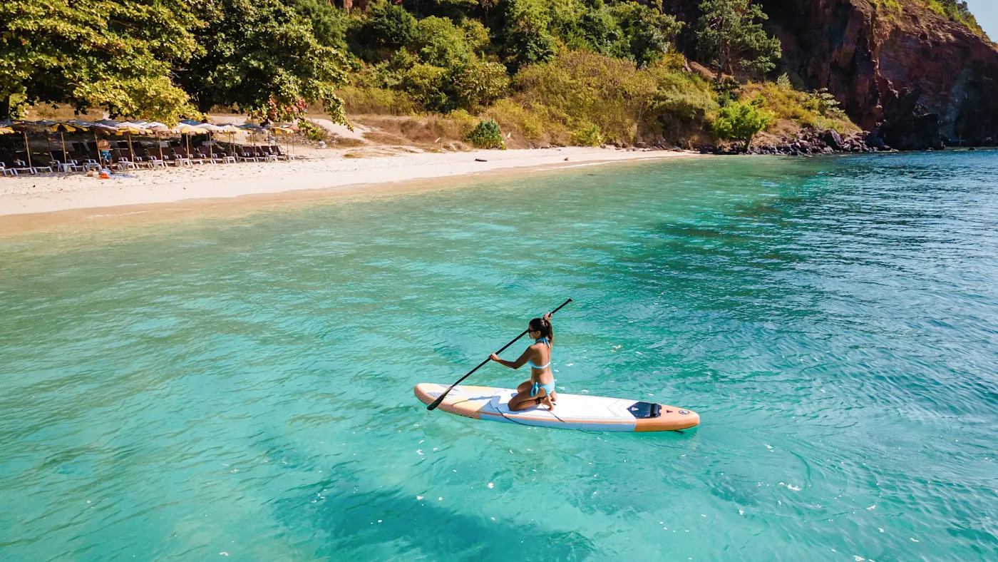 Thaïlande, surf Femme sur une planche de paddle pagayant sur une eau turquoise dans une baie calme avec plage de sable. Thaïlande.
