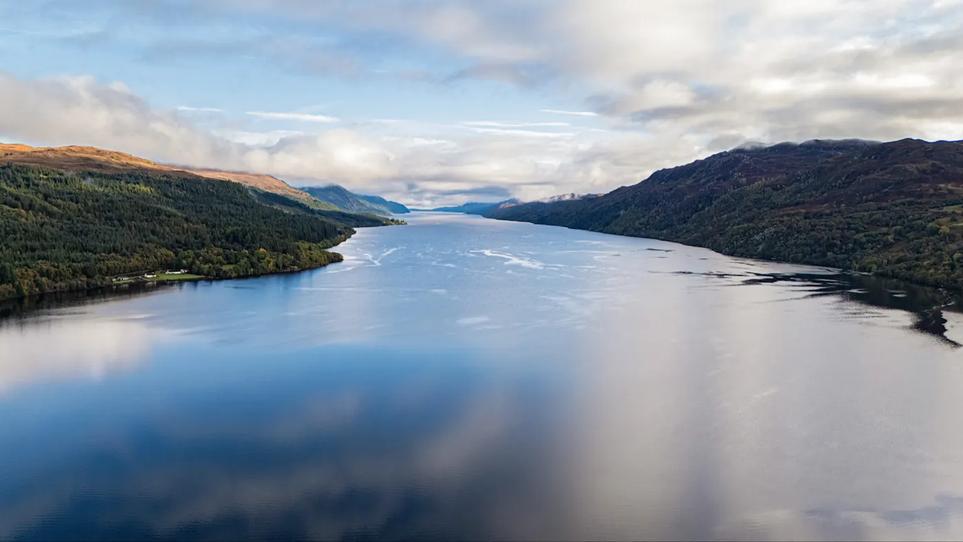 Loch Ness, Schottland, Vereinigtes Königreich Dramatische Luftaufnahme von Loch Ness umgeben von grünen Hügeln und bewölktem Himmel. Loch Ness, Schottland, Vereinigtes Königreich.