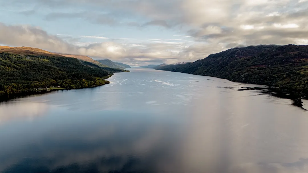 Dramatische Luftaufnahme von Loch Ness umgeben von grünen Hügeln und bewölktem Himmel. Loch Ness, Schottland, Vereinigtes Königreich.