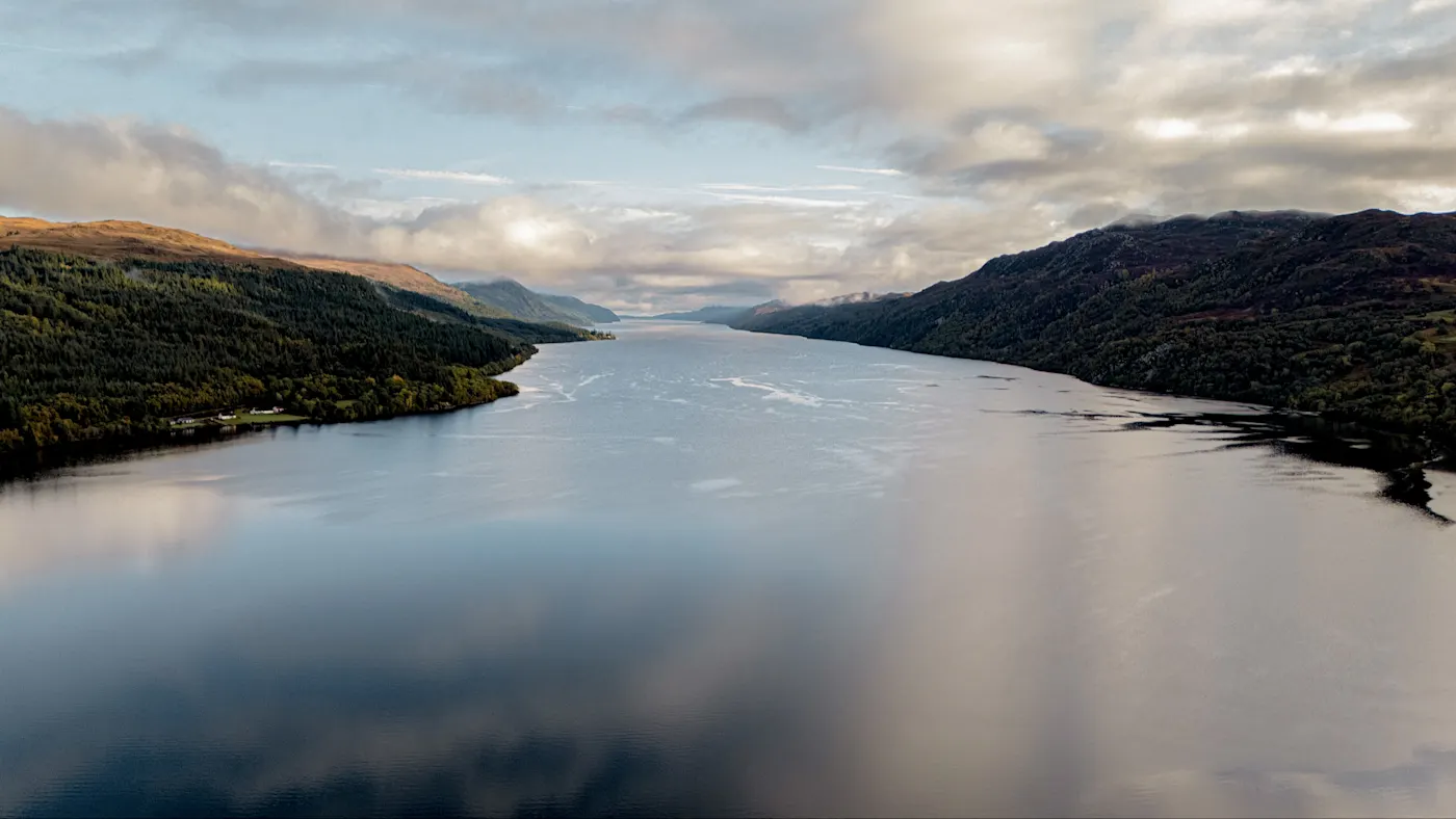 Dramatische Luftaufnahme von Loch Ness umgeben von grünen Hügeln und bewölktem Himmel. Loch Ness, Schottland, Vereinigtes Königreich.