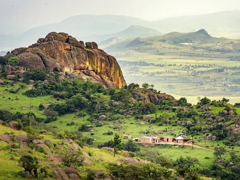 Südafrika, Grünes Tal Landschaft mit riesigem Granitfelsen und traditionellen Hütten im grünen Tal. Südafrika.