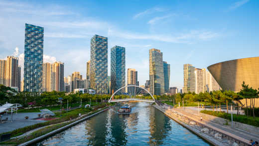 Ausflugsdampfer auf einem Kanal in Incheon mit Skyline im Hintergrund, aufgenommen im Songdo-Park