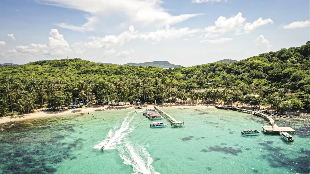 Tropischer Strand mit Palmen, kristallklarem Wasser und Booten am Pier. Phu Quoc, Vietnam.
