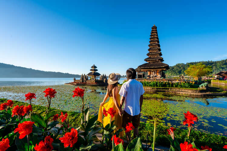 Fleurs rouges et couple qui contemple un vieux temple sur un petit lac lors d'un voyage de noces en Indonésie