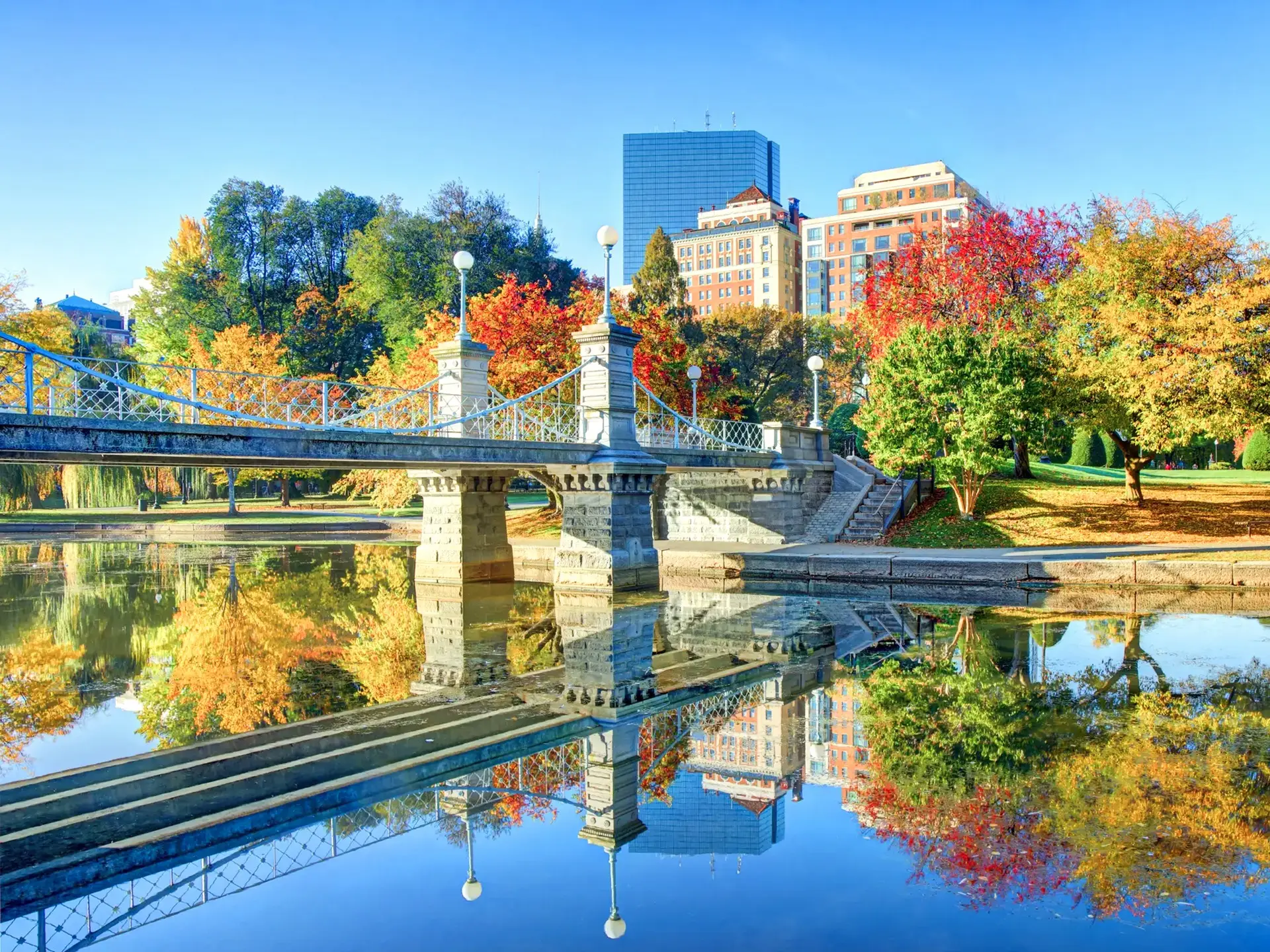 Herbstliche Bäume spiegeln sich im Wasser nahe einer Brücke. Boston, Massachusetts, USA.
