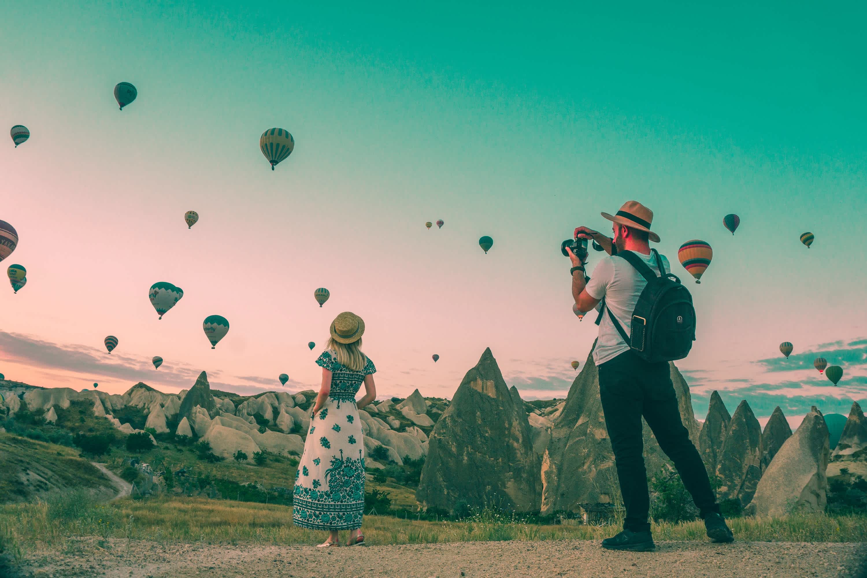 Un couple de voyageurs au milieu du magnifique désert de Cappadoce en Turquie survolé par des dizaines de montgolfières au coucher du soleil.