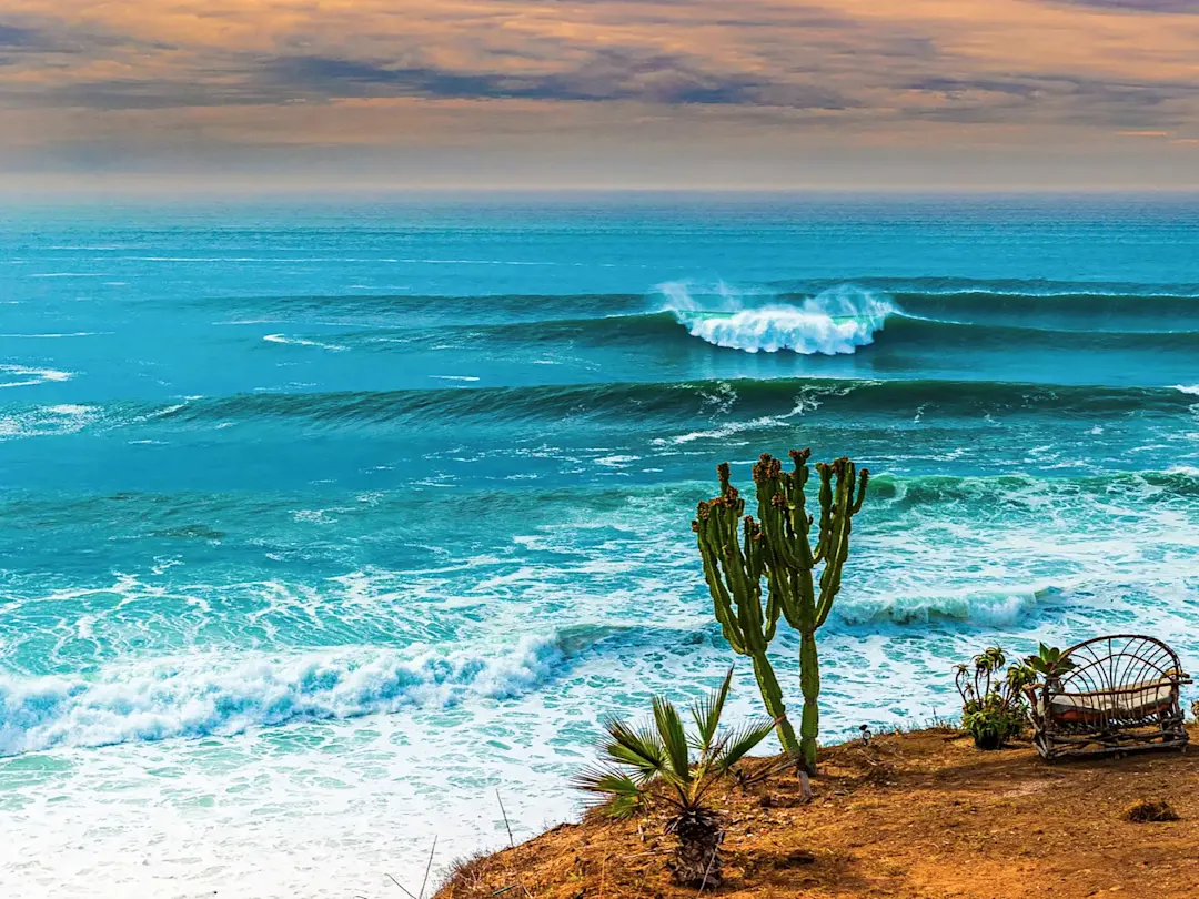 Wellen brechen an der Küste mit Kakteen und Sitzbank. Todos Santos, Baja California Sur, Mexiko.
