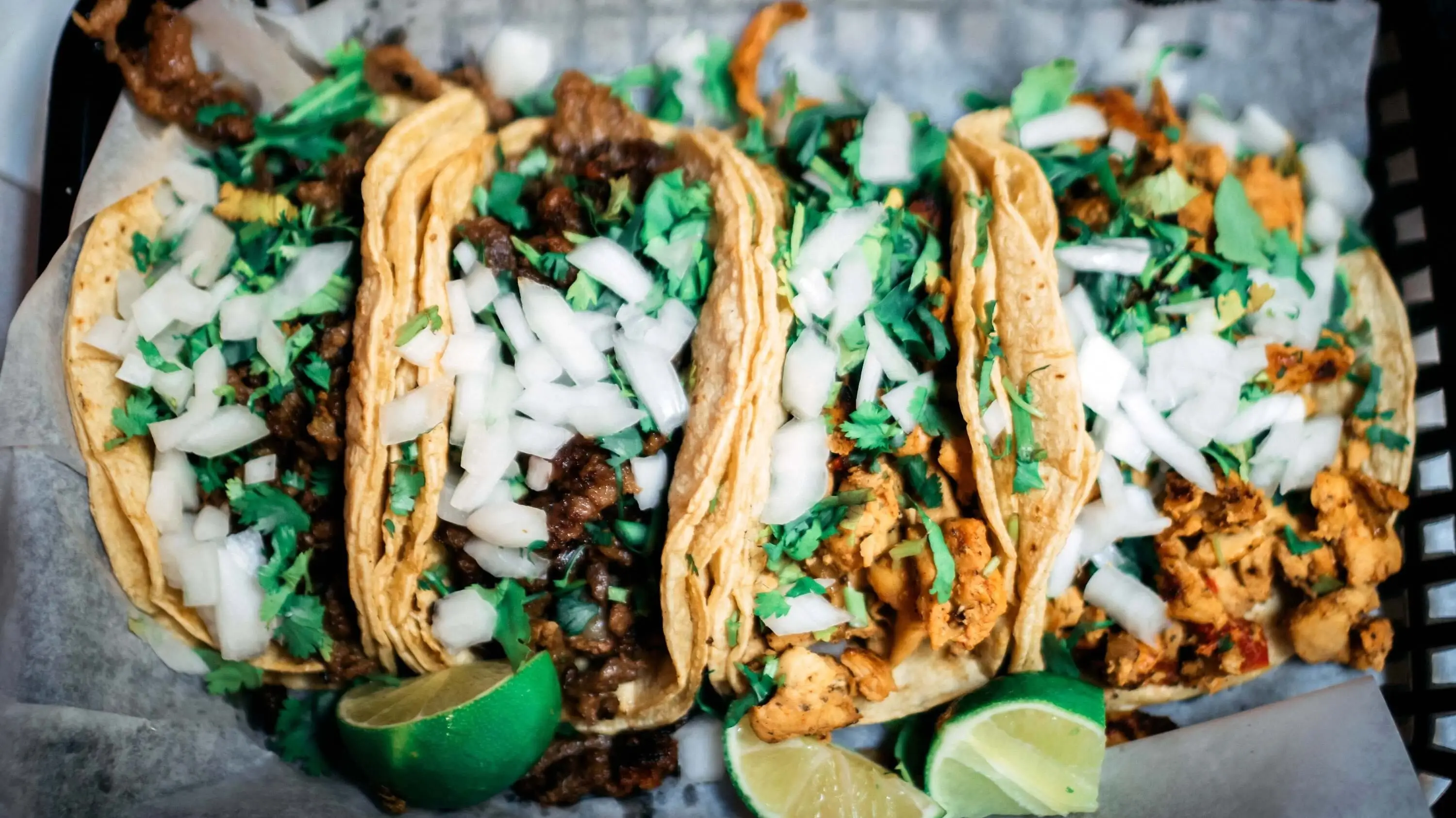mexico pic Drei Tacos, gefüllt mit gehacktem Fleisch, Zwiebelwürfeln und frischem Koriander, werden in einem mit Papier ausgelegten Korb serviert, mit Limettenspalten an der Seite.