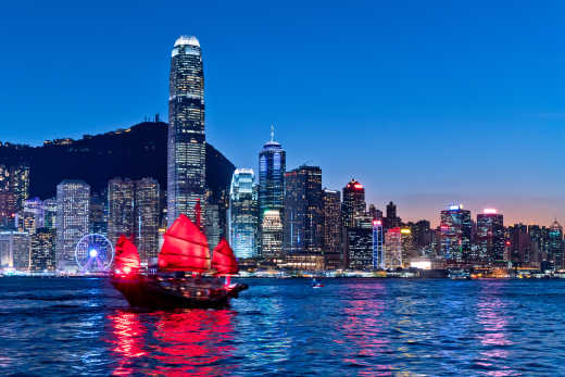 Vue sur Victoria Harbour à Hong Kong, dans l'obscurité, avec une jonque à voiles rouges au premier plan