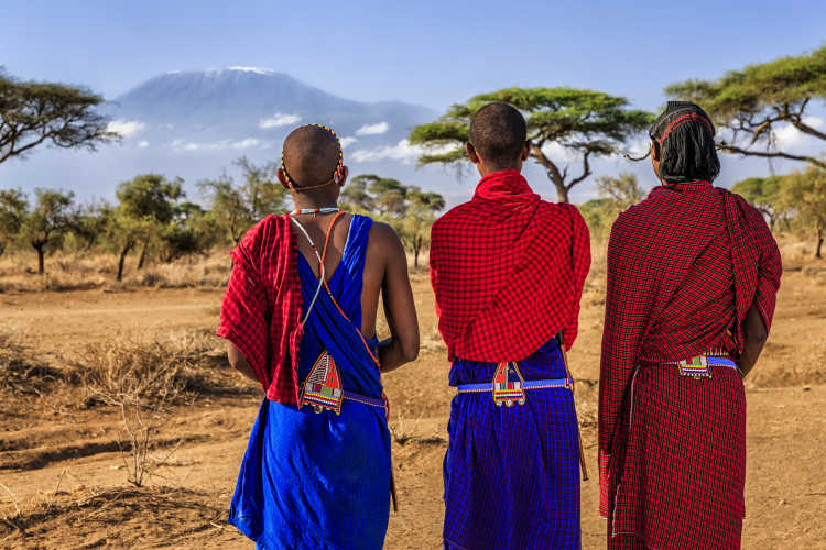 Drei kenianische Frauen in der Savanne mit Berg im Hintergrund.