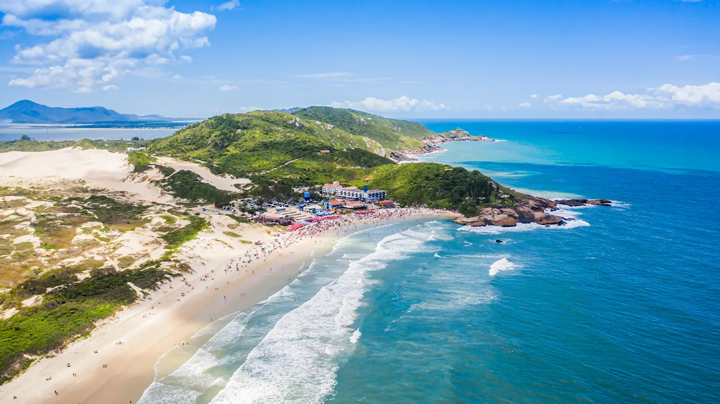 Brasilien, Santa Catarina, Florianópolis Luftaufnahme eines belebten Strandes mit Sanddünen und grünen Hügeln. Florianópolis, Santa Catarina, Brasilien.