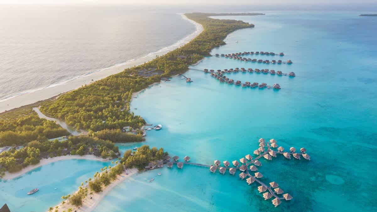 Vue aérienne de la magnifique île de Bora Bora et ses habitations sur pilotis installées en pleine mer, dans lesquelles vous aurez peut-être la chance de séjourner pendant votre voyage en Polynésie française.
