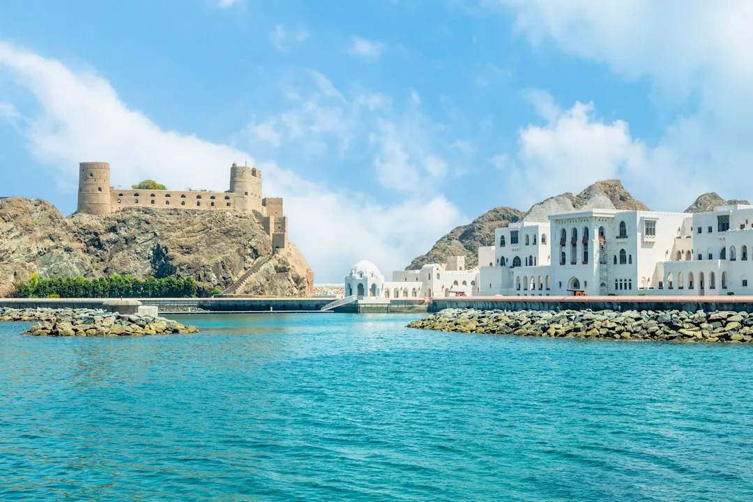 Blick auf die arabische Burg Al Jalali, die auf den Felsen und weißen königlichen Palastgebäuden steht, Muscat, Oman.


