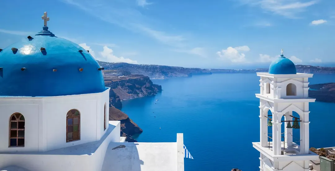 Luftaufnahme der ikonischen blau-weißen Gebäude von Santorin, mit atemberaubendem Blick auf die tiefblaue Ägäis, die sich weit bis zum Horizont erstreckt.