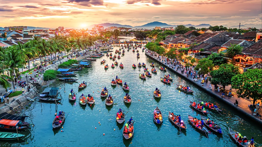 Bunte Boote auf dem Fluss bei Sonnenuntergang, gesäumt von historischen Gebäuden. Hoi An, Vietnam.
