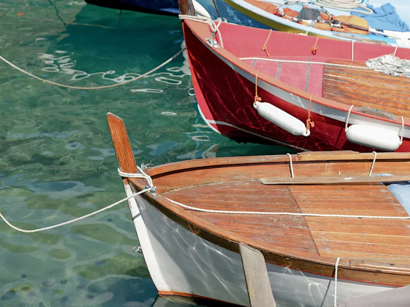 Rote und weiße Holzboote auf klarem, türkisfarbenem Wasser in einem Hafen, Ligurien, Italien.