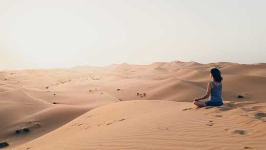 Junge Frau meditiert in der Wüste während des Sonnenuntergangs.

