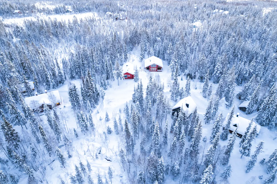 Traditionelle Holzhütten im verschneiten Wald, Luftaufnahme, Finnland
