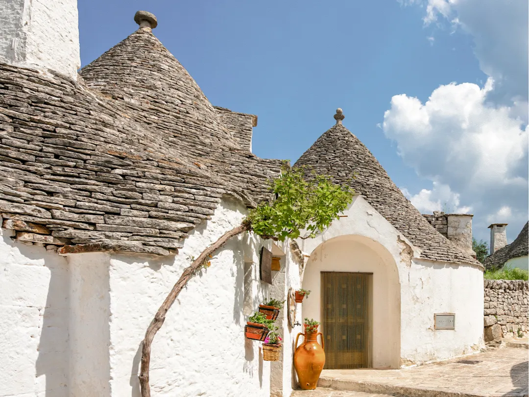 Traditionelle Trulli-Häuser mit weißen Wänden und kegelförmigen Dächern unter blauem Himmel, Alberobello, Italien.