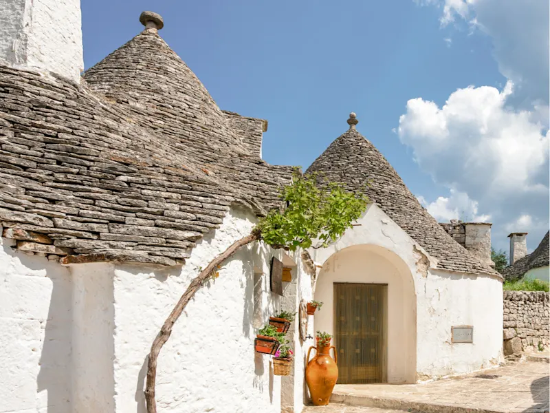 Traditionelle Trulli-Häuser mit weißen Wänden und kegelförmigen Dächern unter blauem Himmel, Alberobello, Italien.