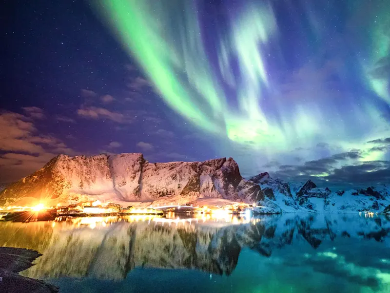 Nordlicht über verschneiten Bergen und Fjordspiegelung. Reine, Nordland, Norwegen.