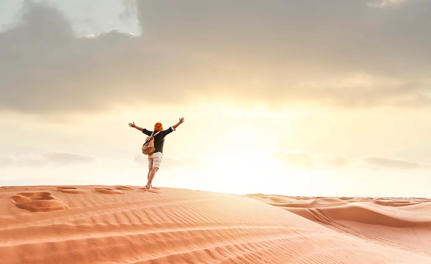 Homme pieds nus sur une dune de sable au coucher du soleil, bras tendus, Oman, désert